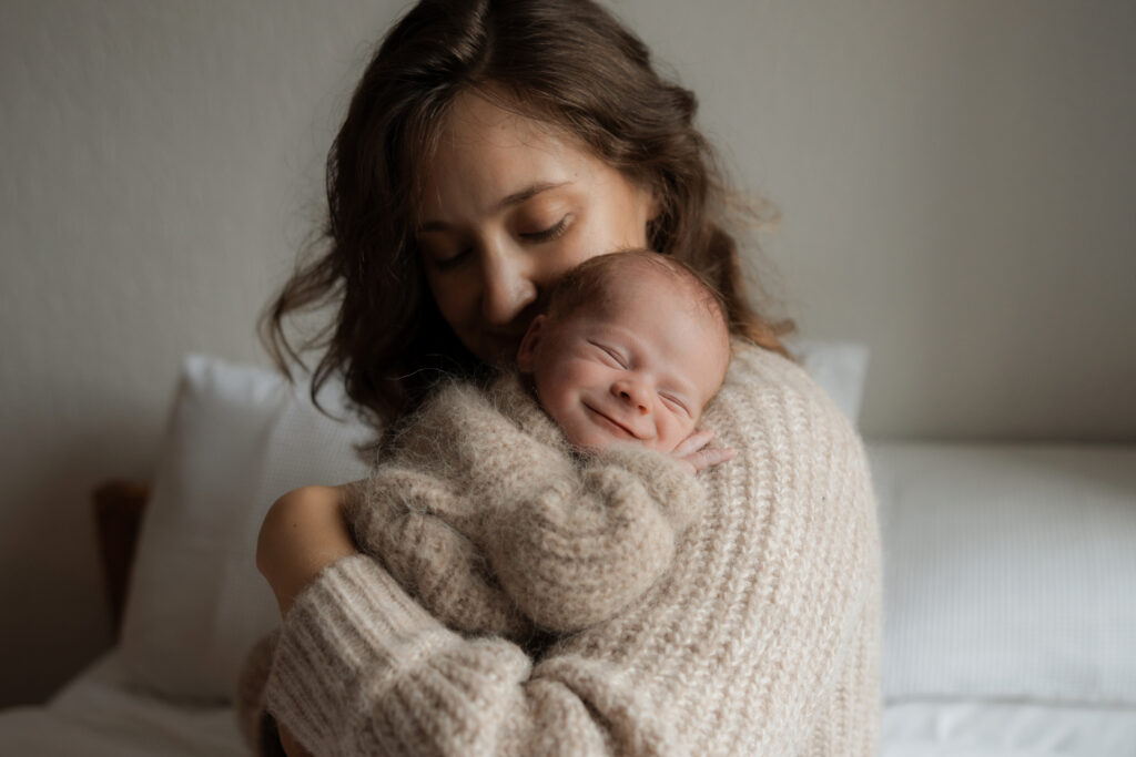 mother cradling her smiling newborn baby on her shoulder in her home