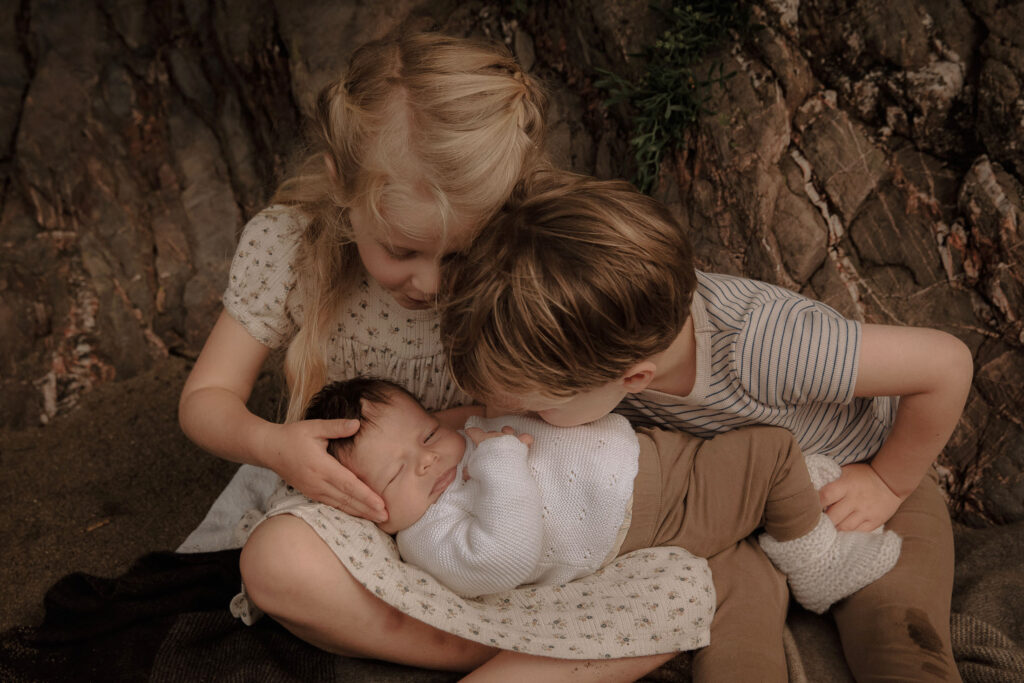 newborn baby cradled by his two siblings on the beach
