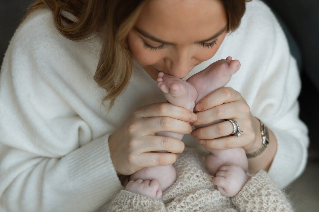 mother tenderly kissing her newborn baby's feet